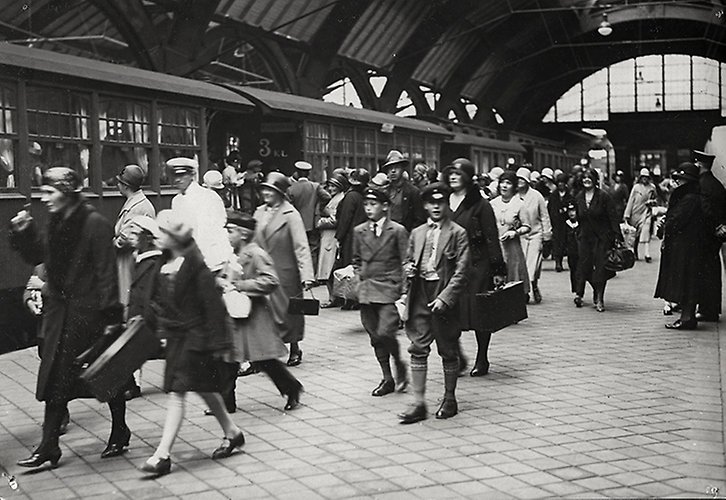 Svartvitt foto av människor som går med resväskor bredvid ett tåg.