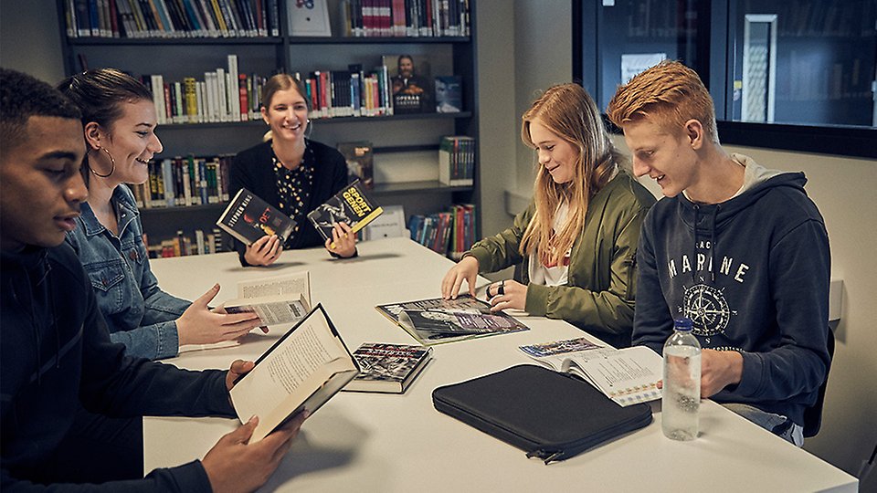 Fyra elever och en lärare sitter och arbetar i biblioteket tillsammans med en lärare.