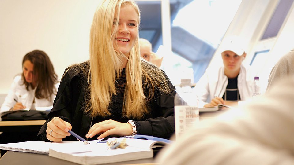 En långhårig blond elev sitter vid sin bänk och småskrattar.