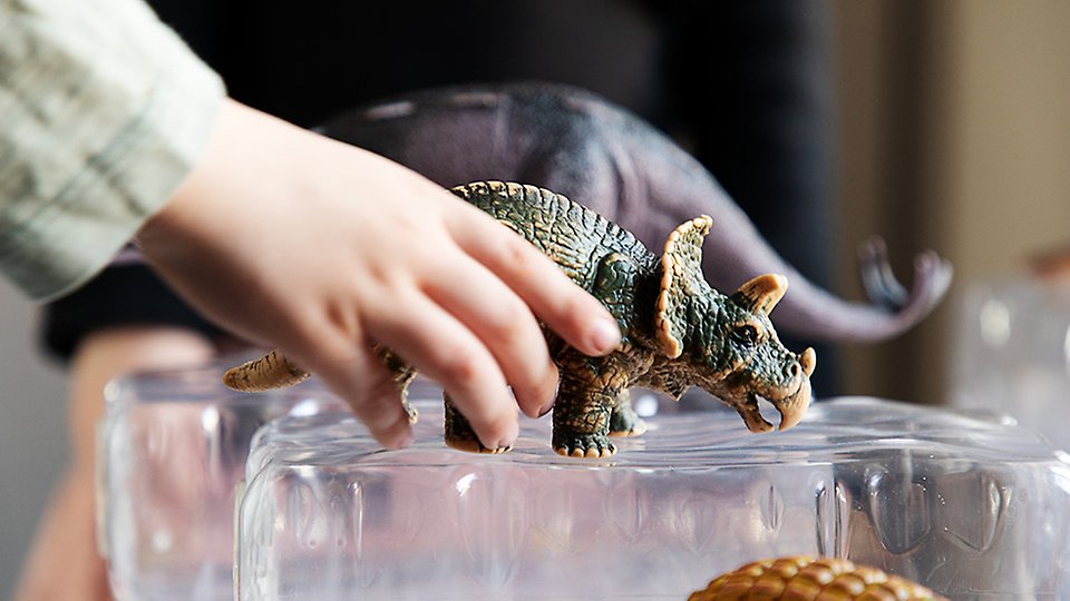 Närbild på en barnhand som håller i en dinosaurie.