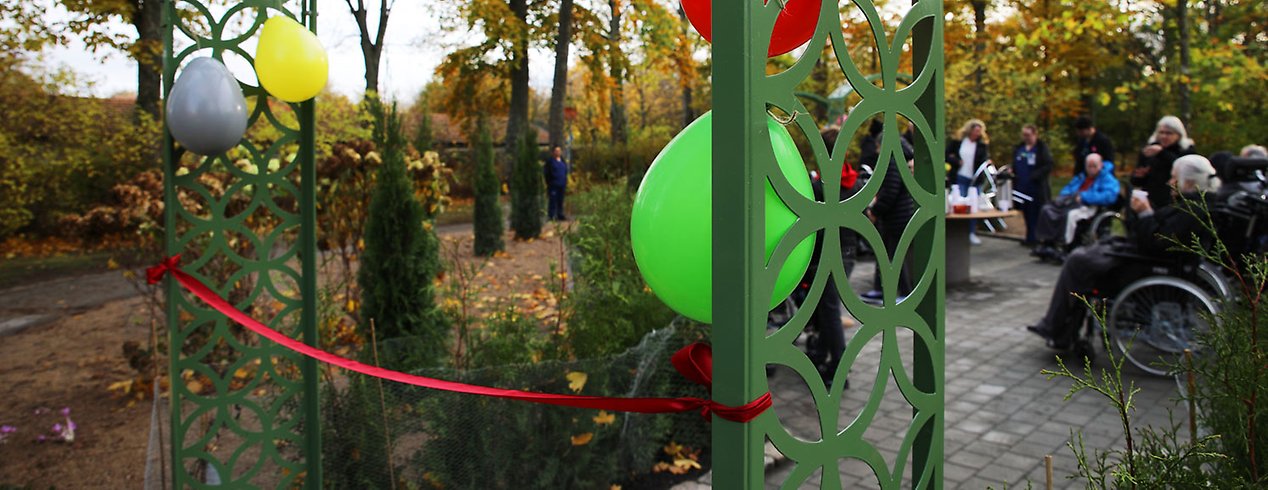 Ingången till trädgården är prydd av ballonger och de boende har samlats vid det nybyggda bordet.