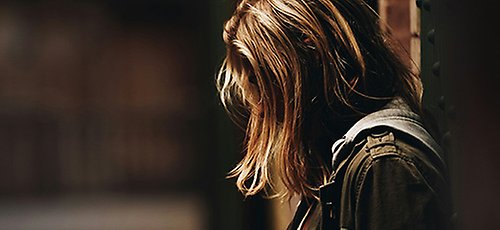 Ensam ung kvinna i profil står och tittar ner i marken.