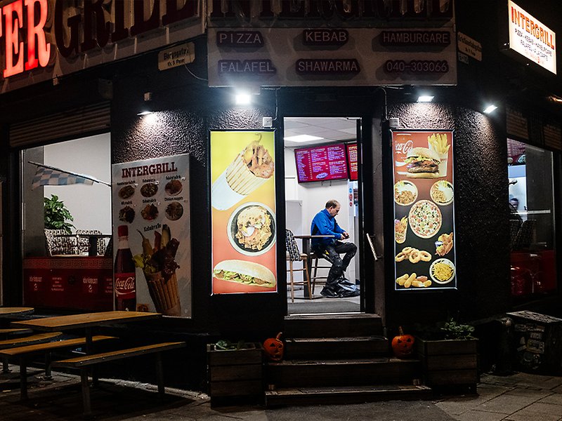 Inter Grill fotograferad från utsidan, i mörkt kvällsljus. Inne i restaurangen sitter en person.