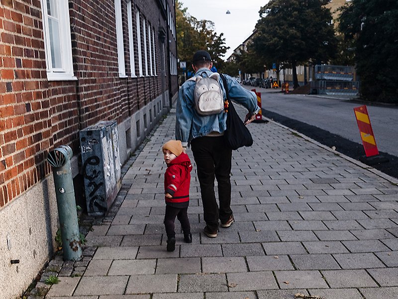 En vuxen person och ett barn går på en trottoar och håller hand.