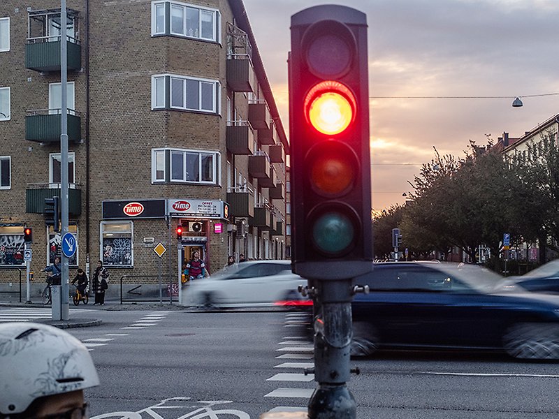 Rött trafikljus vid korsningen Ystadsgatan/Nobelvägen. Bilar susar förbi och personer väntar på att gå över övergångsstället.