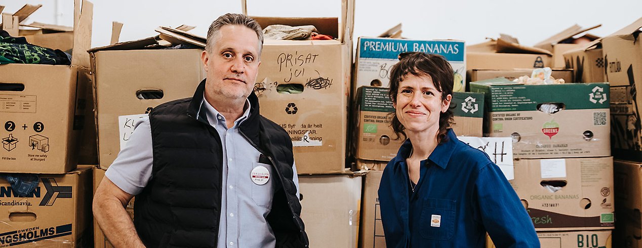 Philip har ljusblå skjorta och svart väst. Emilie är klädd i blå overall. De står framför flyttkartonger med prylar.