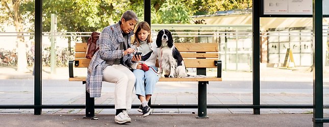 Kvinna, barn och hund sitter tillsammans i en busskur.