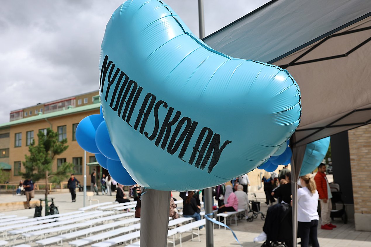 Blå ballong med texten Nydalaskolan. I bakgrunden står människor på skolgården. 