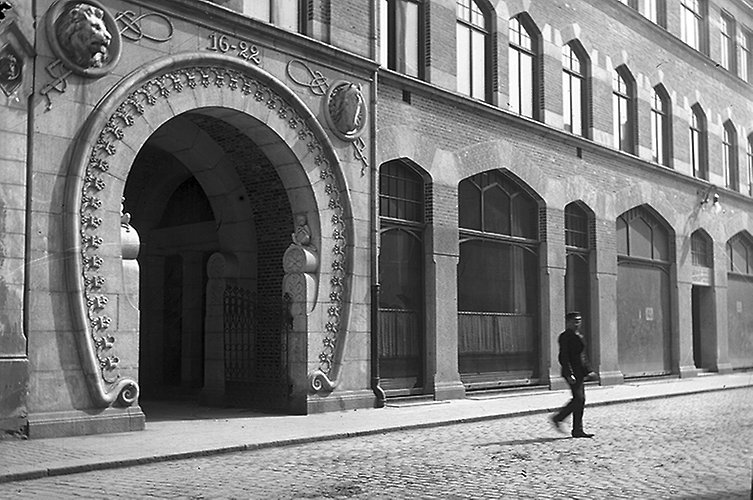 Fasad med smal trottoar, ingången är rundad med en dekorativ båge runtom. 