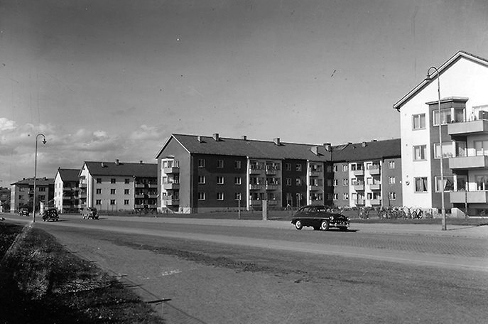 Gata med fyra bilar, hyreshus i bakgrunden.