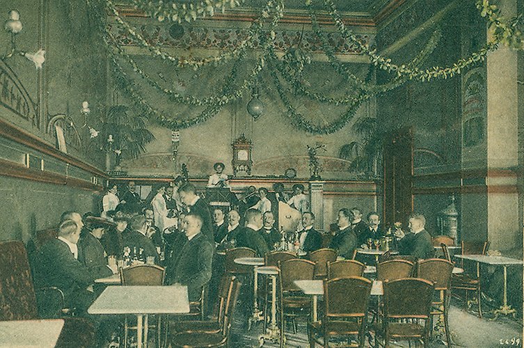 Färglagt foto med män i kostym vid bord. Girlander i taket.