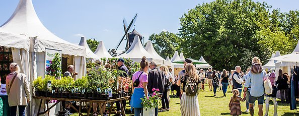 Personer går i en park bland försäljare av växter under ett trädgårdsarrangemang.