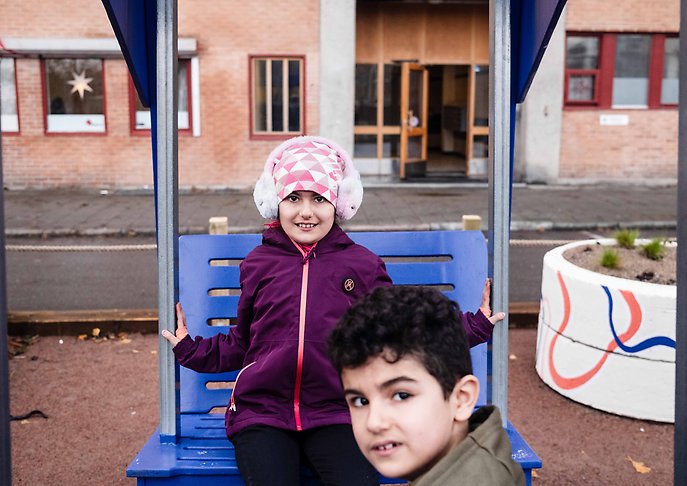 Två barn ler mot kameran lekandes på en gunga på skolgatan på Friisgatan.