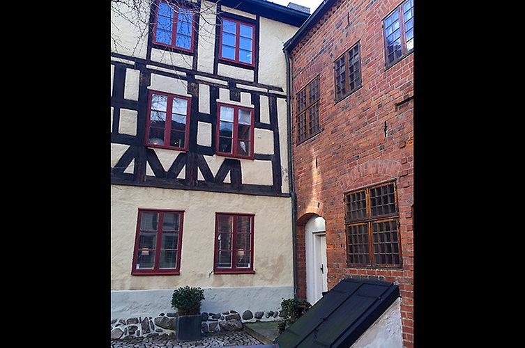 Fasad på två äldre hus. Ett i rött tegel och ett korsvirkeshus i ljus puts.