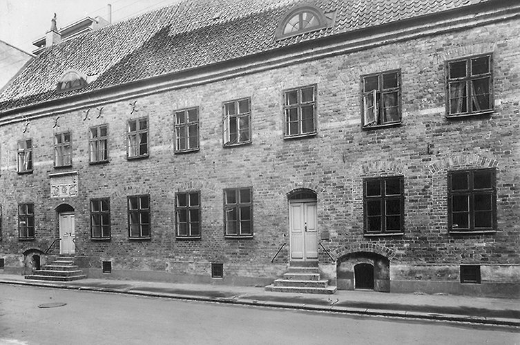 Äldre svartvitt foto på långt tegelhus i två våningar.