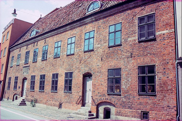 Äldre färgfoto på långt tegelhus i två våningar.