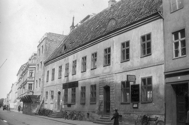 Äldre svartvitt foto på långt putsat hus i två våningar.