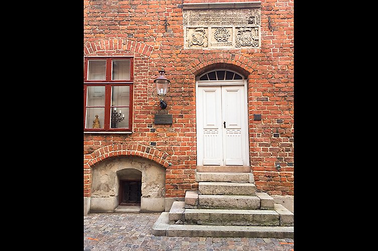 Fasad på äldre rött tegelhus med en trappa upp till en vit dörr.