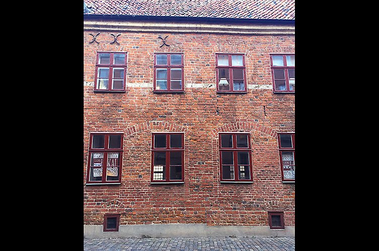 Fasad på äldre rött tegelhus. Många fönster. 