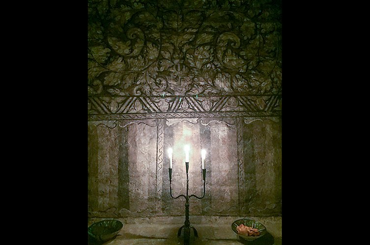 Äldre vägg med fina dekorationer. Tända ljus i en kandelaber i förgrunden. 