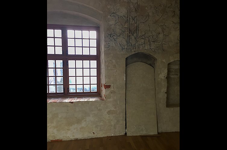 Vägg och fönster i gammalt hus. Spår av väggdekorationer syns. 