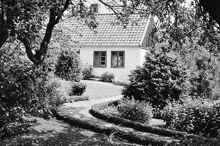 Äldre svartvitt foto med ljust pitoreskt hus och vacker trädgård.
