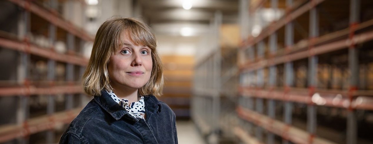 En person står i en stor tom lagerlokal och tittar in i kameran. Personen ler lite.