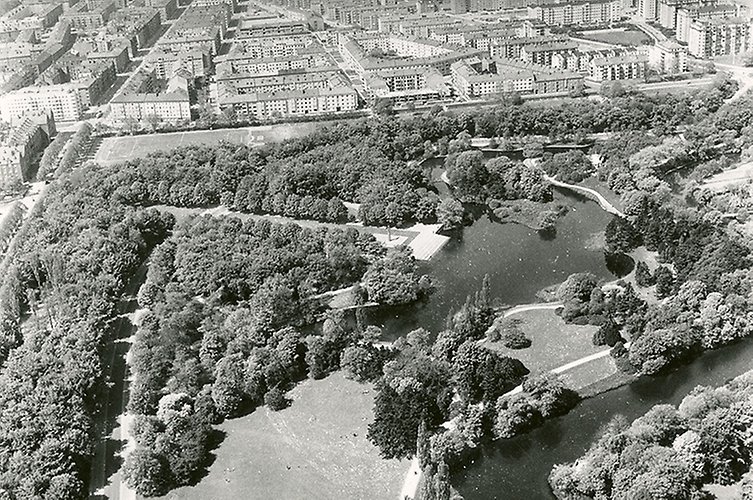 Äldre svartvitt flygfoto över parkområde med stad i horisonten. 