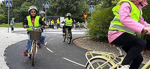 Barn i västar som cyklar på asfalt.