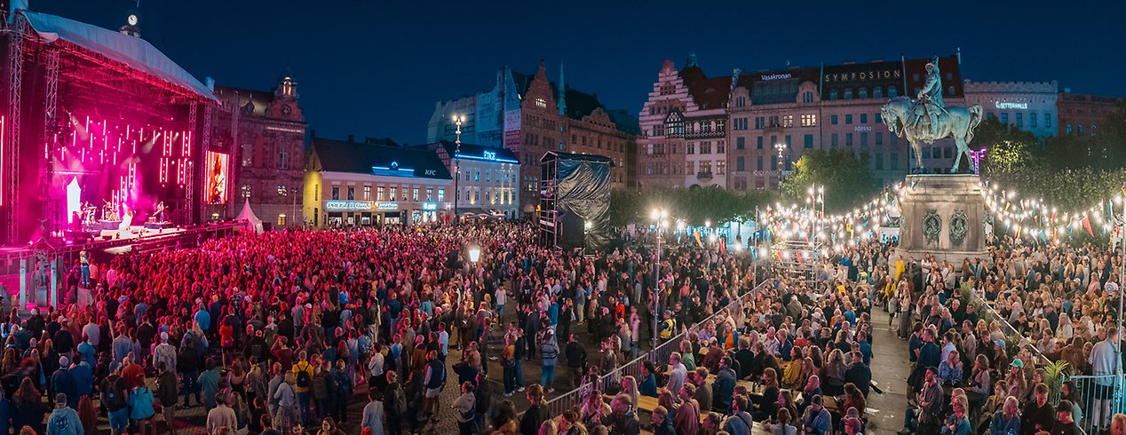 Ett publikhav framför en stor scen på ett torg, kvällstid.