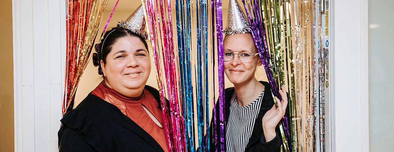 Charlotta och Helena står under ett glitterdraperi med partyhattar på huvudet.