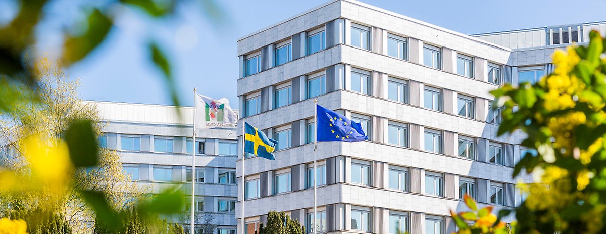 Malmö stads stadshus. Utanför står tre flaggstänger med en Malmö stad flagga, en Sverigeflagga och en EU-flagga.