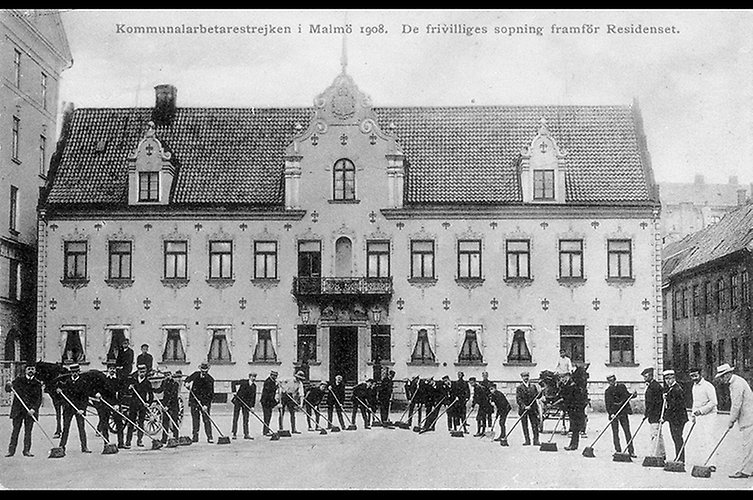 Personer med sopborstar framför stort hus.