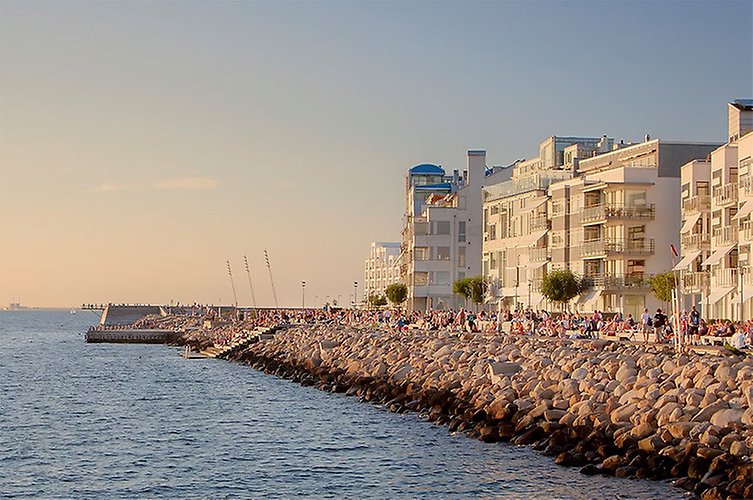 Strandpromenad vid havet med mycket människor och ljusa byggnader i bakgrunden.