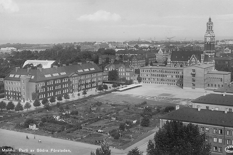 Svartvitt foto med vy över större byggnader och en kyrka.