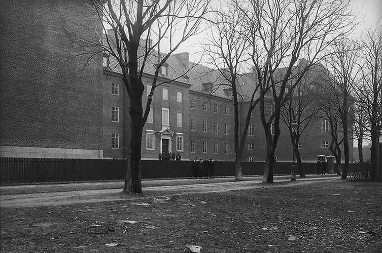 Gammalt svartvitt foto på skolbyggnad i tegel. Inga löv på träden.