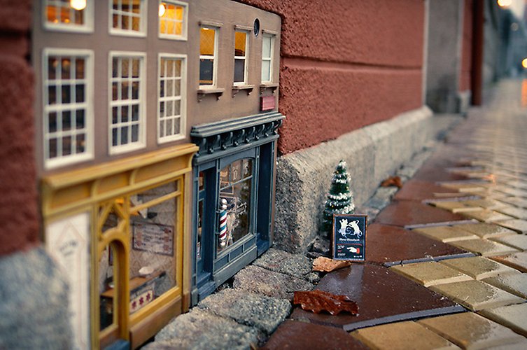 Miniatyrhus med frisör insprängt i den nedre delen av fasaden till ett bostadshus. Utanför står en julgran. 