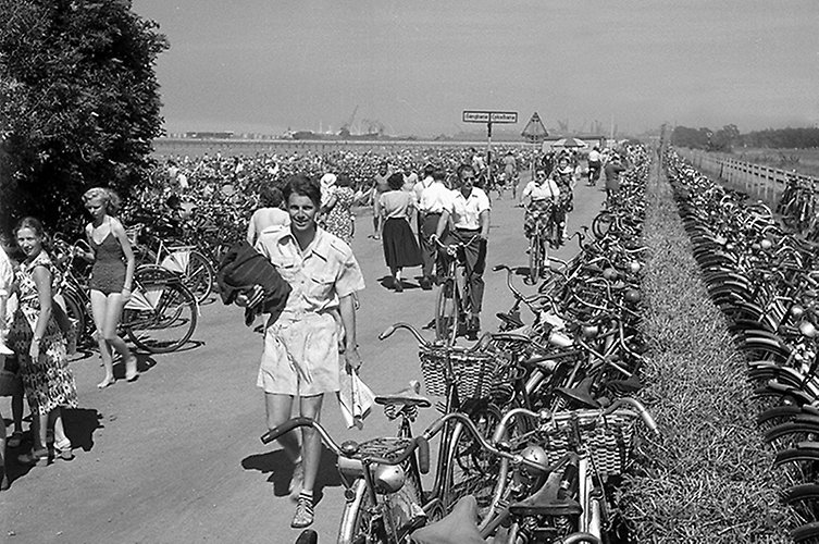 Äldre foto. Cykelbana vid havet. Många cyklar och sommarklädda fotgängare. 