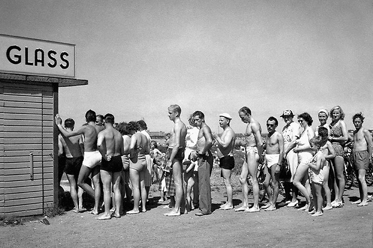 Äldre foto. Lång kö till glasskiosk. Många i badkläder. 