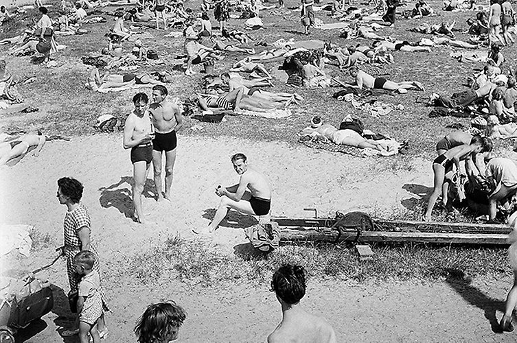 Äldre svartvitt foto. Strand fylld med badgäster. 