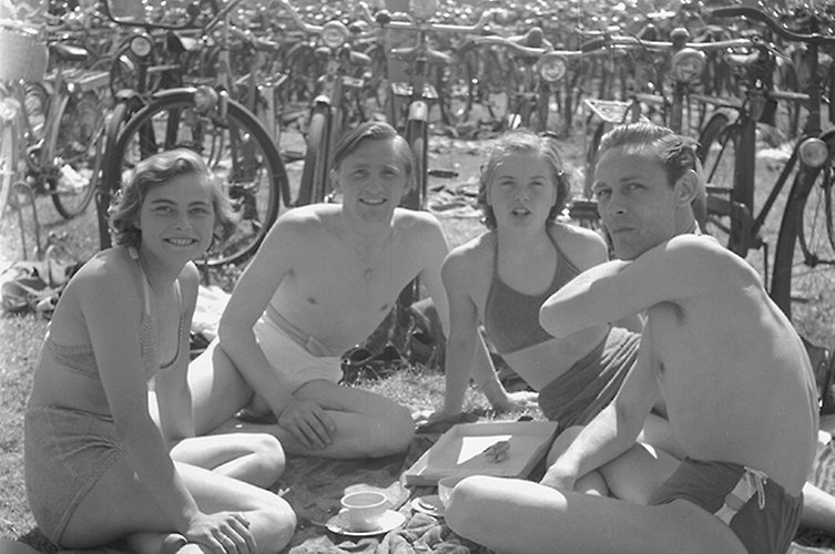 Äldre svartvitt foto. Fyra unga personer i badkläder ler mot kameran. Cyklar i bakgrunden. 
