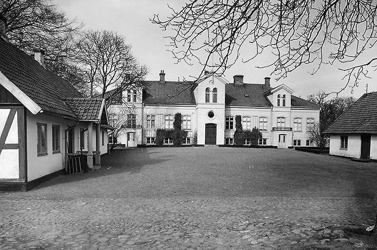 Gammalt foto. Herrgård och tillhörande hus med en tom gårdsplan i förgrunden.