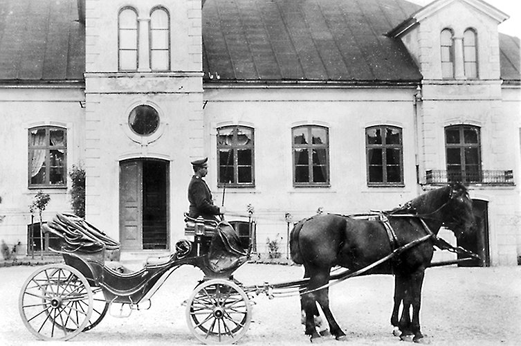 Äldre svartvitt foto.Häst och vagn med kusk utanför en fin byggnad.