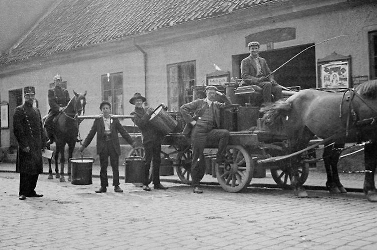 Bild från 1908 som visar en polisövervaknad latrintömning på Skälbogatan. På bilden syns en häst som drar en vag och 5 män framför ett vitt hus. 