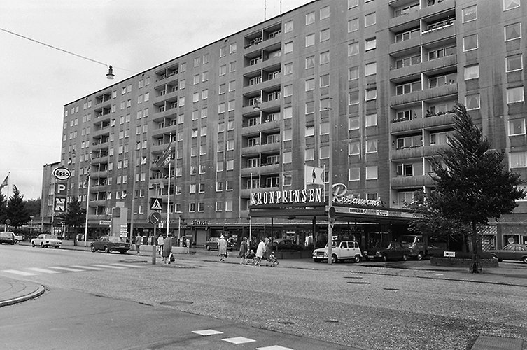 10-våningshus med 5 trappuppgångar, i bottenplan butikslokaler och en entréingång med pelare och tak. Äldre foto.