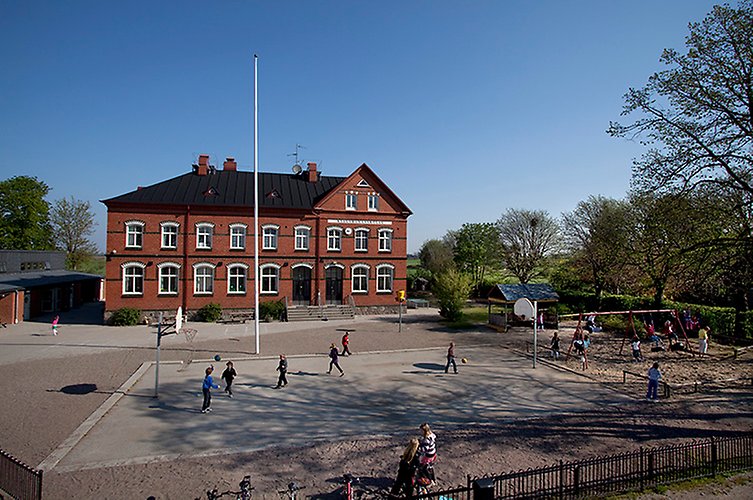 Nytaget foto på den två våningar höga skolan. Barn leker på skolgården.