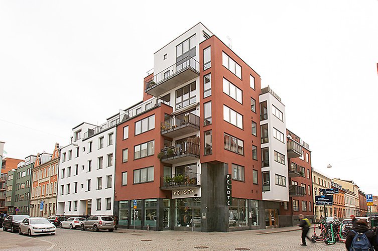Modernt flerfamiljshus med balkonger och restauranglokal i bottenplan. Bredvid äldre fastigheter. 