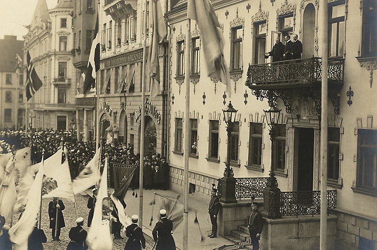 Personer studentmössor framför balkongen.
