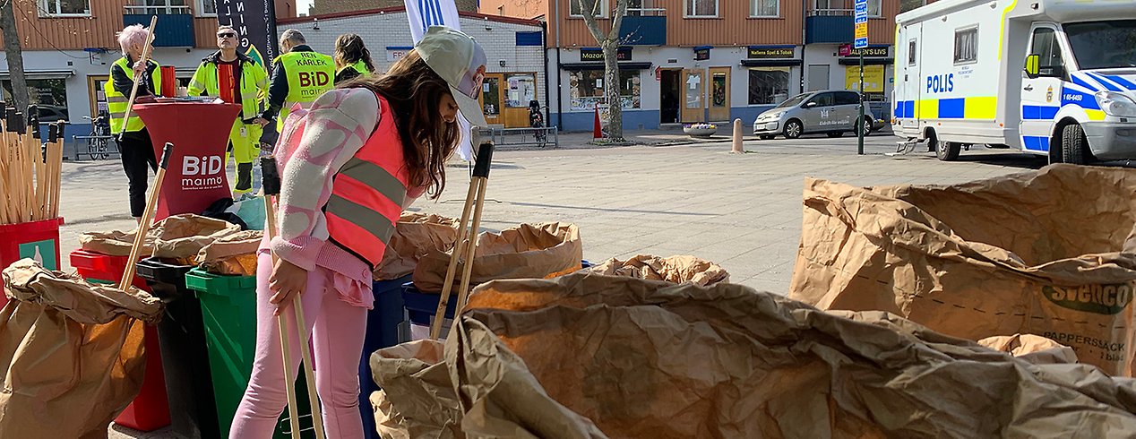 En flicka i rosa varselväst släpper ner skräp i stora avfallssäckar på ett torg i Malmö. 