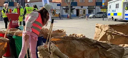 En flicka i rosa varselväst och rosa byxor sorterar skräp i stora papperssäckar på ett torg i Malmö. 